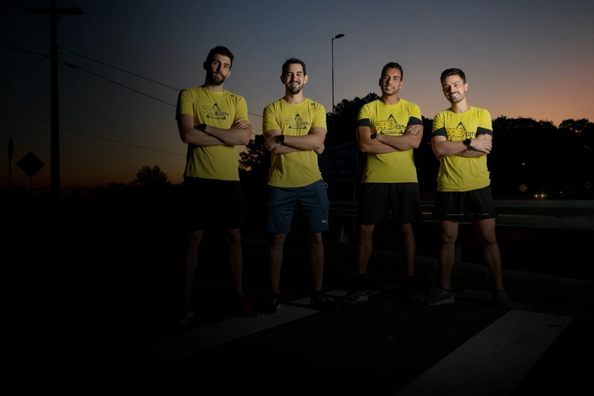 Os quatro profissionais da ProElite de braços cruzados, de camiseta amarela, ao anoitecer