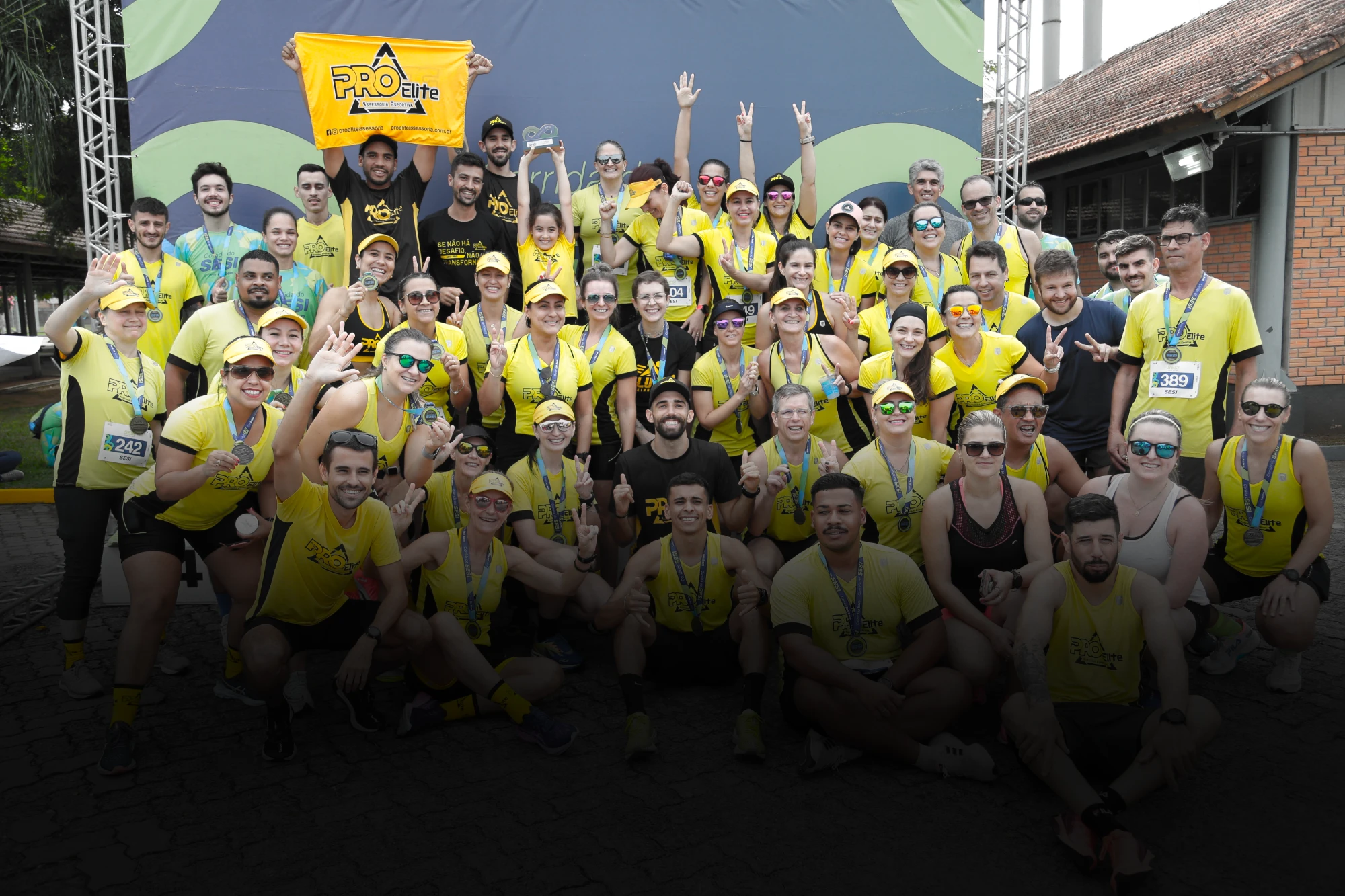 Alunos da ProElite comemorando com medalhas depois de uma prova, com a bandeira da assessoria erguida